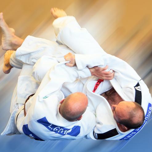 Zwei Judokämpfer führen einen Wurf in weißen Gis aus, während sich der Hintergrund unscharf darstellt.