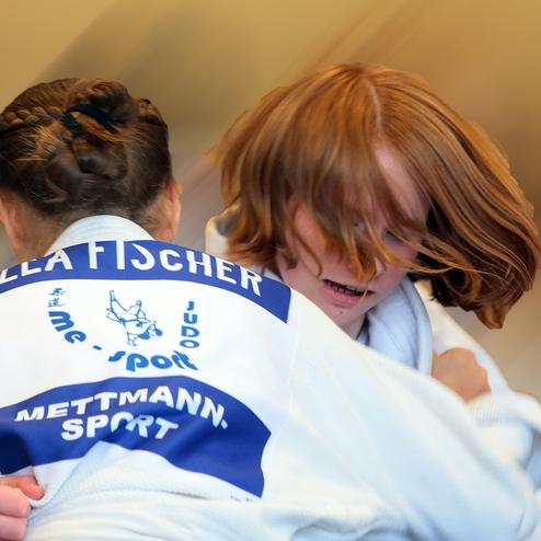 Zwei Judokas in weißen Gi kämpfen, während eine Person mit roten Haaren im Fokus steht.