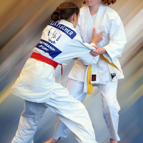 Zwei Judokas in Wettkampfkewrls sparen mit weißen Judogis, eine hat einen roten, die andere einen gelben Gürtel.