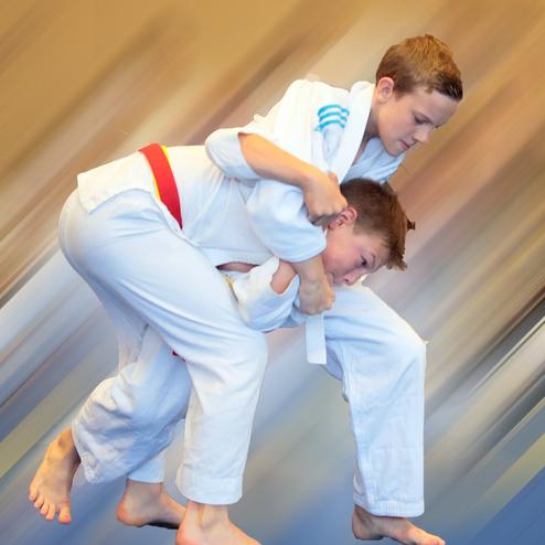 Zwei Kinder im Judoanzug führen einen Wurf im Training aus, während sie in Bewegung sind.