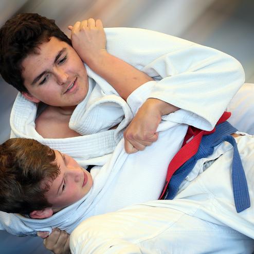 Zwei Jungen in Judo-Anzügen kämpfen miteinander, einer trägt einen roten, der andere einen blauen Gürtel.