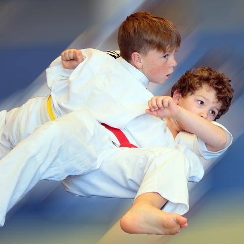 Zwei Kinder in weißen Judogi führen einen Wurf im Judotraining aus, während sie auf einer blauen Matte landen.