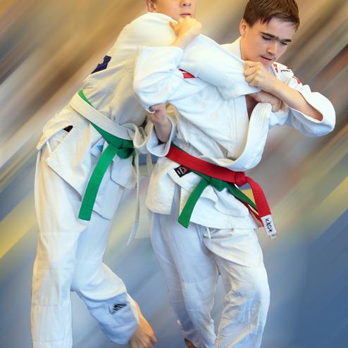 Zwei Jugendliche in weißen Judo-Gis kämpfen im Stand, einer hält den anderen im Würgegriff.