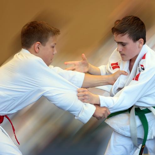 Zwei Jugendliche in Judogis üben Techniken, während sie sich beim Wettkampf entgegenkommen.