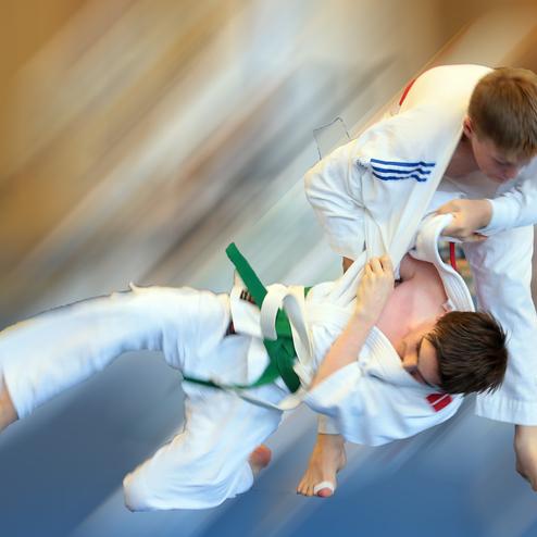 Zwei Judoka in weißen Anzügen führen einen Wurf auf einer blauen Matte aus, einer mit grünem Gürtel.