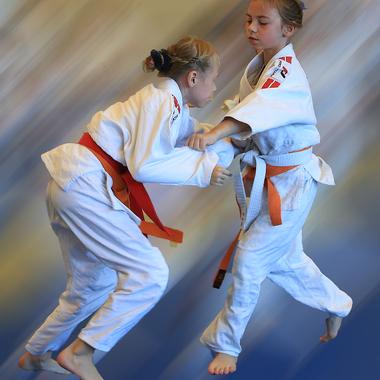 Zwei Kinder im Judoanzug stehen in Bewegung, während sie einander greifen und kämpfen.