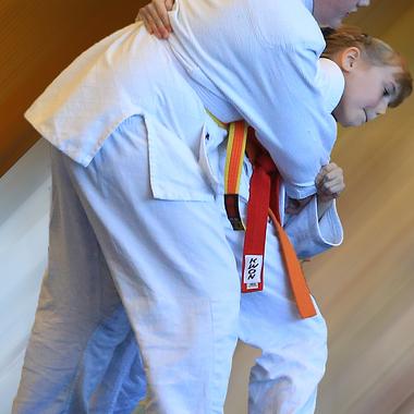 Zwei Kinder im Judoanzug üben einen Wurf, einer hält den anderen im Griff. Hintergrund unscharf.