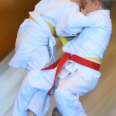 Zwei Kinder in Judogewändern führen einen Hebelgriff während eines Trainings aus. Hintergrund mit Bewegungseffekt.