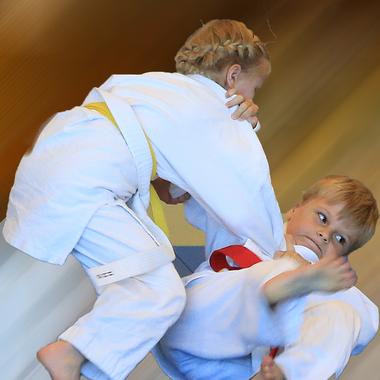 Zwei Kinder im Judoanzug führen einen Wurf im Training durch, eines wird in die Luft gehoben.