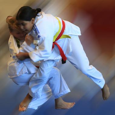 Zwei Kinder in Kampfanzügen führen einen Wurf im Judo aus, mit unscharfem Hintergrund, der Bewegung suggeriert.