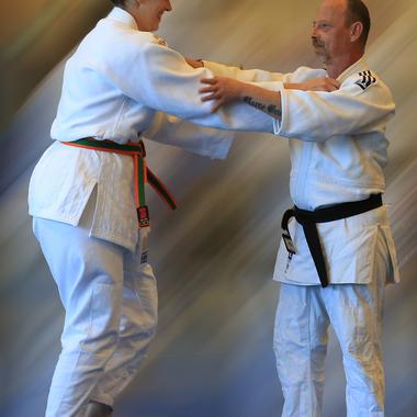 Zwei Personen in Judogi üben eine Technik im Judo. Die Frau hat einen bunten Gürtel, der Mann einen schwarzen Gürtel.