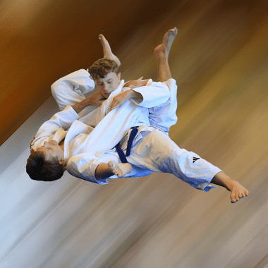 Zwei Judokas in wei&szlig;en Anz&uuml;gen f&uuml;hren einen Wurf aus, w&auml;hrend sie in der Luft schwebend dargestellt sind.