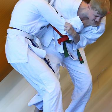 Zwei Sportler in weißen Judokis kämpfen im Stand, einer greift den anderen an und hebt ihn an.