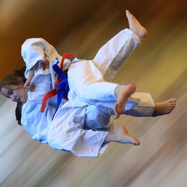 Zwei Judokas in weißen Judoanzügen führen einen Wurf aus, während sich ihre Füße in der Luft befinden.
