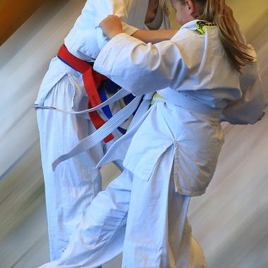 Zwei Kinder in Judoanzügen üben einen Griff, während sie auf einer verschwommenen Hintergrundfläche stehen.