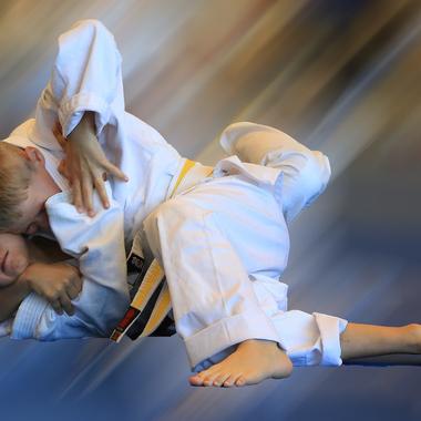 Zwei Kinder in wei&szlig;en Judo-Anz&uuml;gen k&auml;mpfen auf einer blauen Matte im Grappling. Bewegungseffekt durch Unsch&auml;rfe.