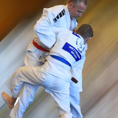 Zwei Judo-K&auml;mpfer in wei&szlig;en Judogis beim Wurf, der erfahrenere K&auml;mpfer hat einen roten G&uuml;rtel, der andere einen blauen.