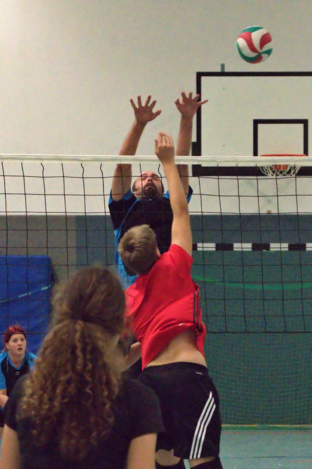 Ein Volleyballspieler springt, um einen Ball über das Netz zu blocken, während ein weiterer Spieler angreift.