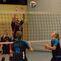 Volleyballspieler in Aktion, ein Spieler springt zur Abwehr des Balls am Netz, andere Spieler warten auf den Ball.