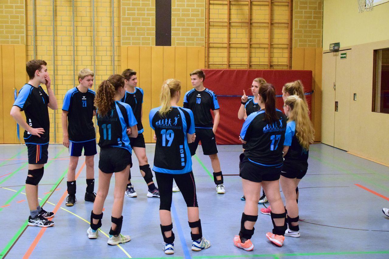 Jugendmannschaft in sportlicher Kleidung diskutiert strategisch in einer Sporthalle mit buntem Bodenmarkierungen.