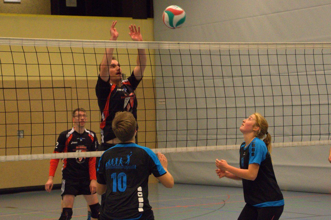 Volleyballspieler in Aktion, ein Spieler springt zur Abwehr des Balls am Netz, andere Spieler warten auf den Ball.