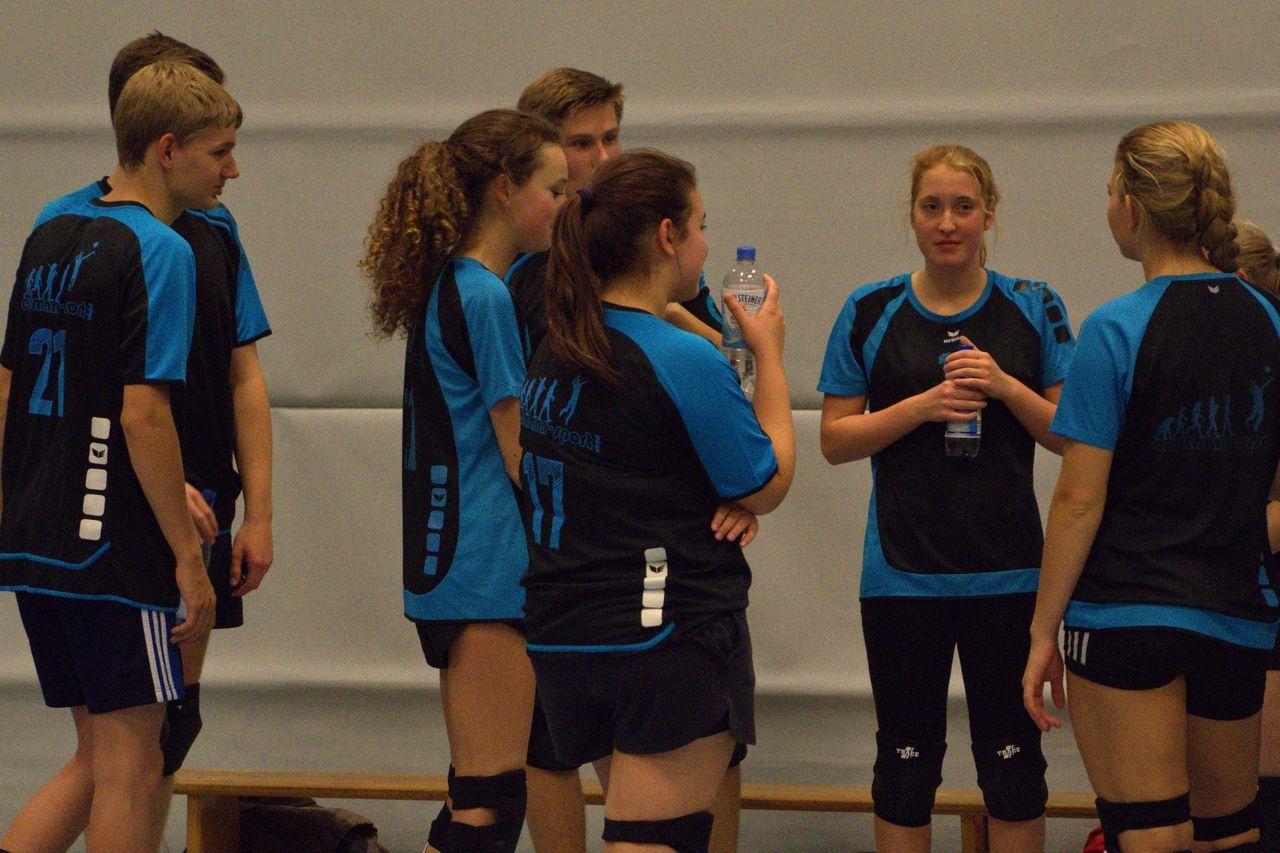 Gruppe von Jugendlichen in Sportkleidung, die sich in einer Sporthalle unterhalten und Wasserflaschen halten.