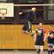 Ein Spieler springt zum Angriff über das Volleyballnetz, während Teamkollegen in sportlicher Kleidung zuschauen.