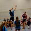 Spielszene eines Volleyballmatches mit Spielern in blauer und roter Sportbekleidung, Netzspannung sichtbar.