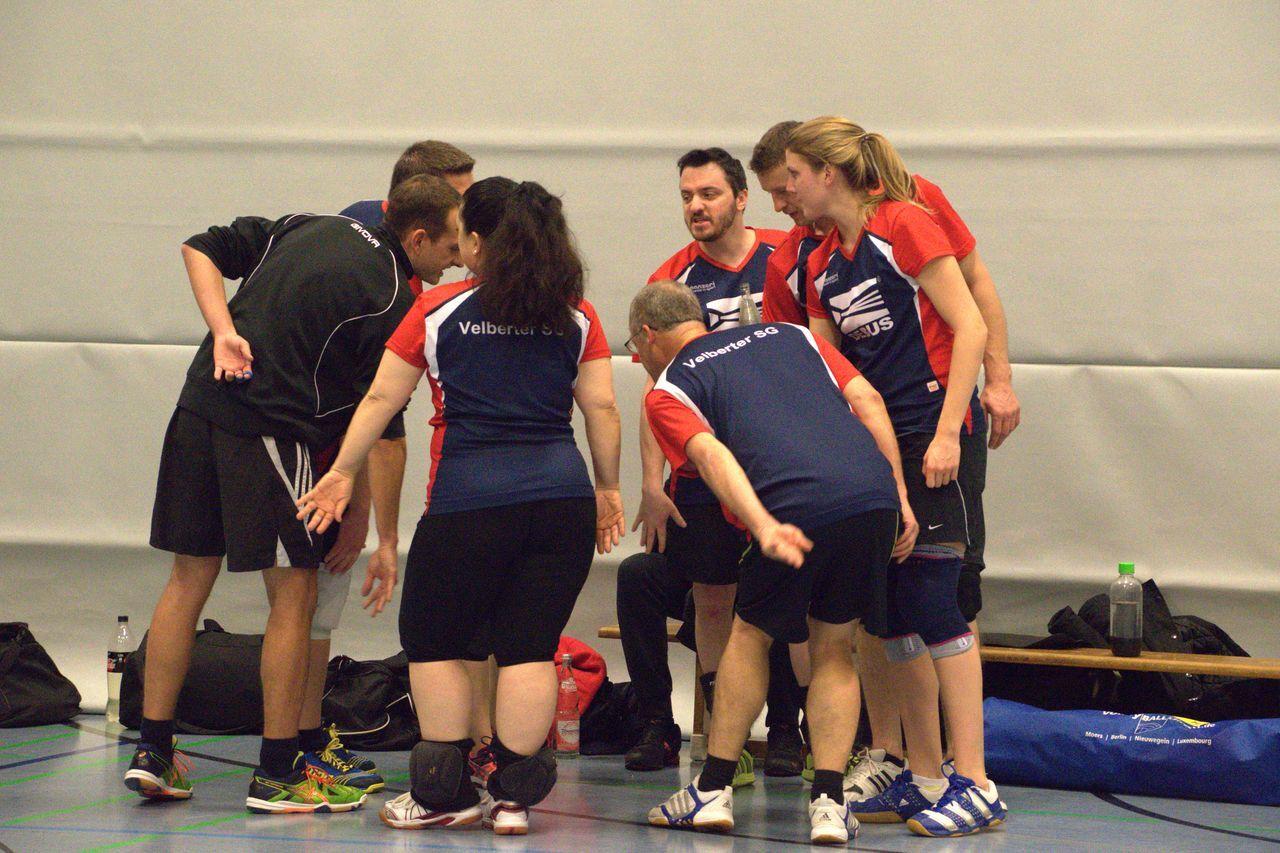 Eine Gruppe von Tischtennisspielern in roten und blauen Trikots diskutiert strategisch im Sportzentrum.