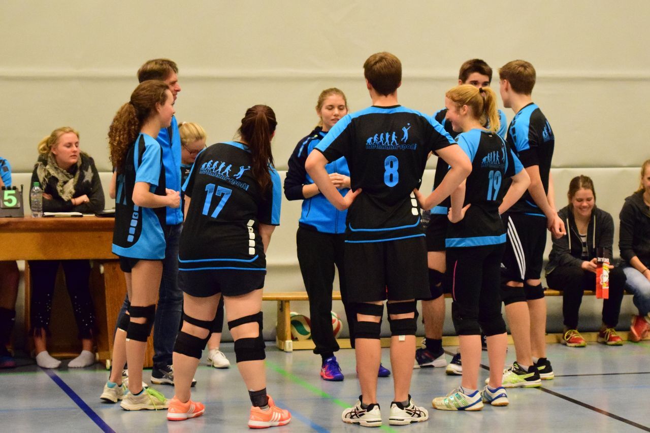 Die Mannschaft bespricht sich während eines Spiels in einer Sporthalle; Spieler tragen schwarze und blaue Trikots.