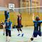 Volleyballspiel mit Spielern in blauen und roten Trikots, während ein Ball über das Netz geschlagen wird.