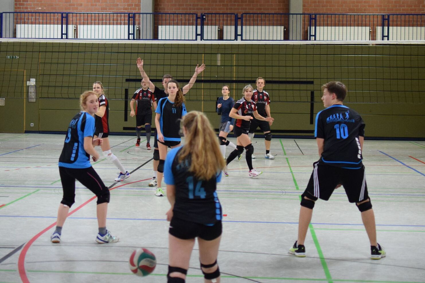 Volleyballspiel in einer Halle mit mehreren Spielern in uniformierten Trikots, ein Ball fliegt zwischen ihnen.
