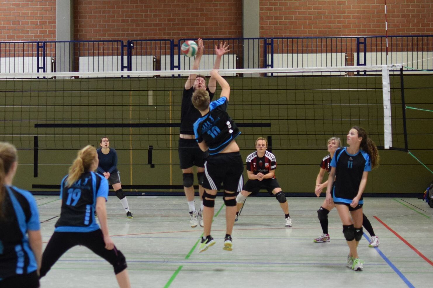 Spielszene mit zwei Volleyballspielern im Sprung, während andere Spieler auf dem Feld positioniert sind.