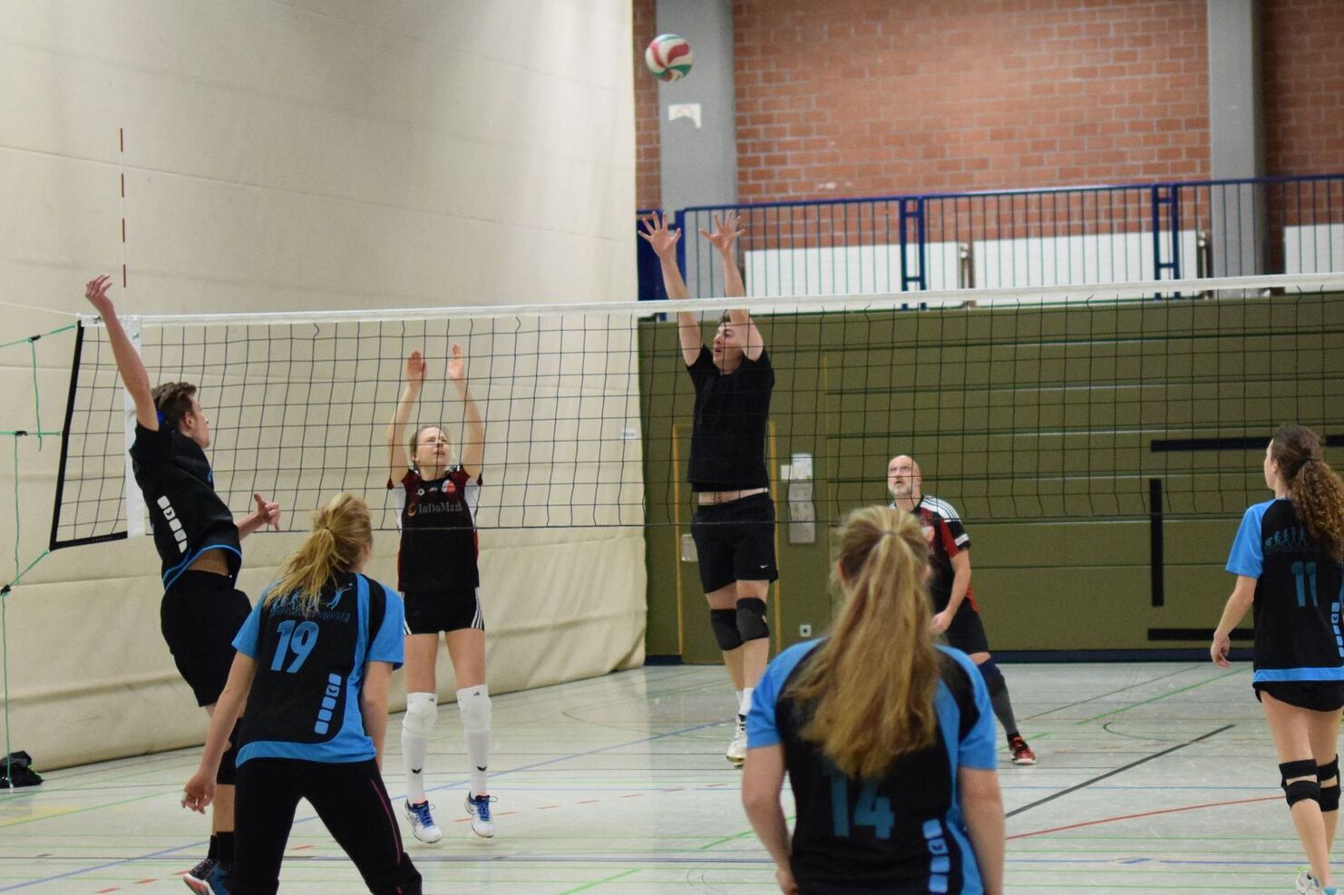 Volleyballspiel in einer Sporthalle mit mehreren Spielern, die den Ball über das Netz annehmen.