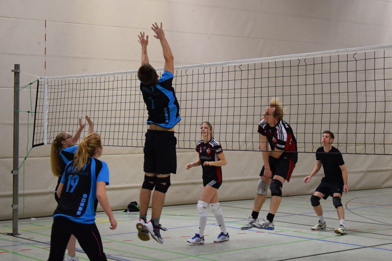 Aktive Volleyball-Spieler springen unter einem Netz, während sie den Ball in einer Sporthalle anspielen.