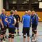Gruppe von sieben Männern in blauen Sporttrikots versammelt sich in einer Sporthalle für eine Teambesprechung.