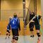 Volleyballspiel mit mehreren Spielern in blauen Trikots, während der Ball über das Netz gespielt wird.