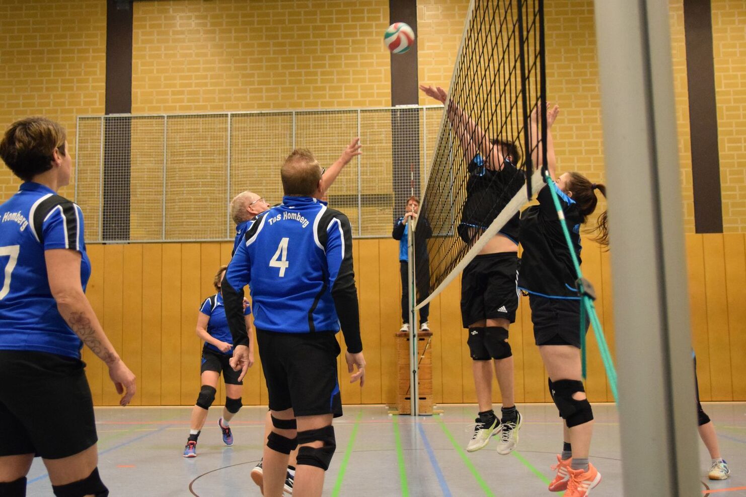 Volleyballspiel mit mehreren Spielern in blauen Trikots, während der Ball über das Netz gespielt wird.