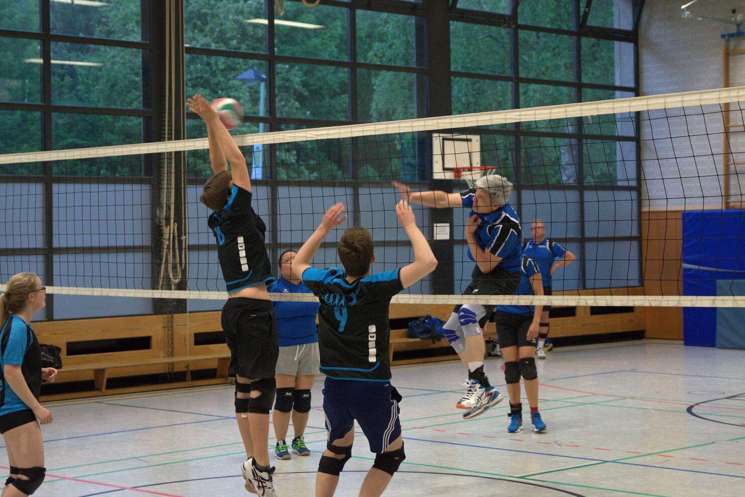 Zwei Volleyballspieler springen hoch, um einen Ball über das Netz zu schlagen, während andere Spieler im Hintergrund warten.