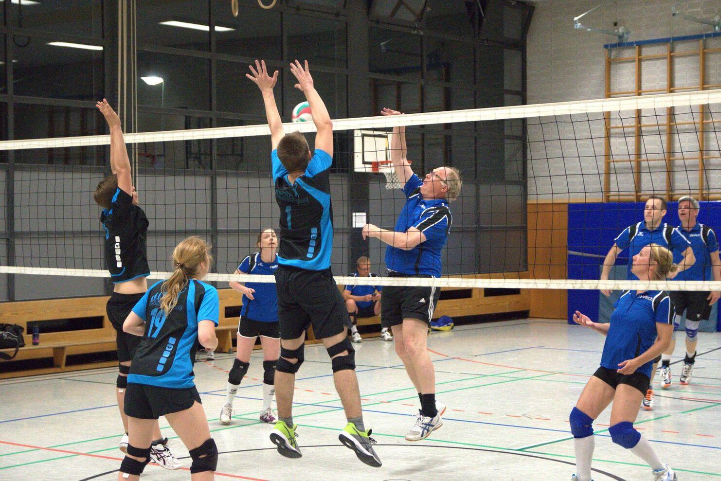 Volleyball-Spieler in blauen Trikots springen hoch, um den Ball über das Netz abzuschlagen.