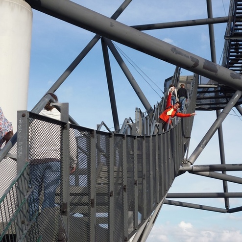 Personen gehen auf einer gewundenen Metalltreppe, die zu einer Aussichtsplattform führt, unter blauem Himmel.