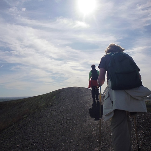 Zwei Wanderer erklimmen einen Hügel auf einem feldweg, der unter einem klaren Himmel verläuft.