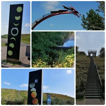 Skulpturen und Informationstafeln zur Astronomie in einer natürlichen Umgebung mit Bäumen und Wasser.