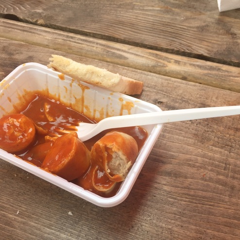 Porree auf einer Holzfläche mit einer Schüssel, die drei Würstchen in Tomatensoße und ein Stück Brot enthält.