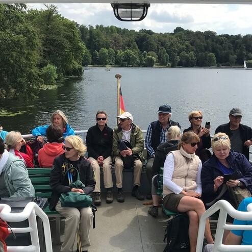 Gruppe von Passagieren auf einem Boot, umgeben von Wasser und Grün, mit Blick auf die Landschaft im Hintergrund.