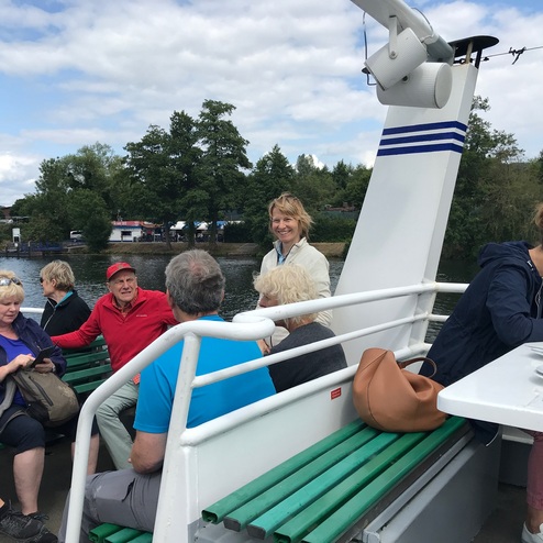 Gruppe von Passagieren auf einem Ausflugsboot, einige unterhalten sich, andere schauen auf ihr Handy oder genießen die Aussicht.