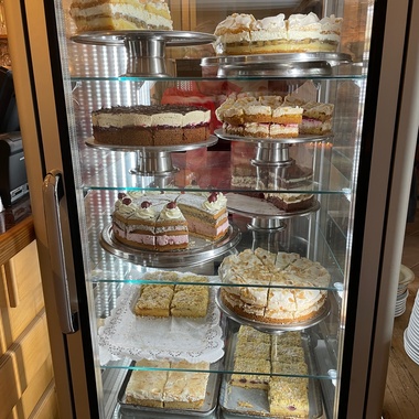 Vitrine mit verschiedenen Kuchensorten, darunter Schichten- und Bienenstichkuchen, dekoriert und appetitlich angerichtet.