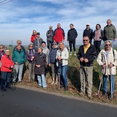 Gruppe von 17 Wanderern mit Stöcken, auf einem Hügel neben einer Straße, bei klaren Himmel und Feldern im Hintergrund.