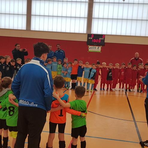 Zwei Gruppen von Kindern in Fußballtrikots stehen in einer Halle, während Trainer ihnen Anweisungen geben.