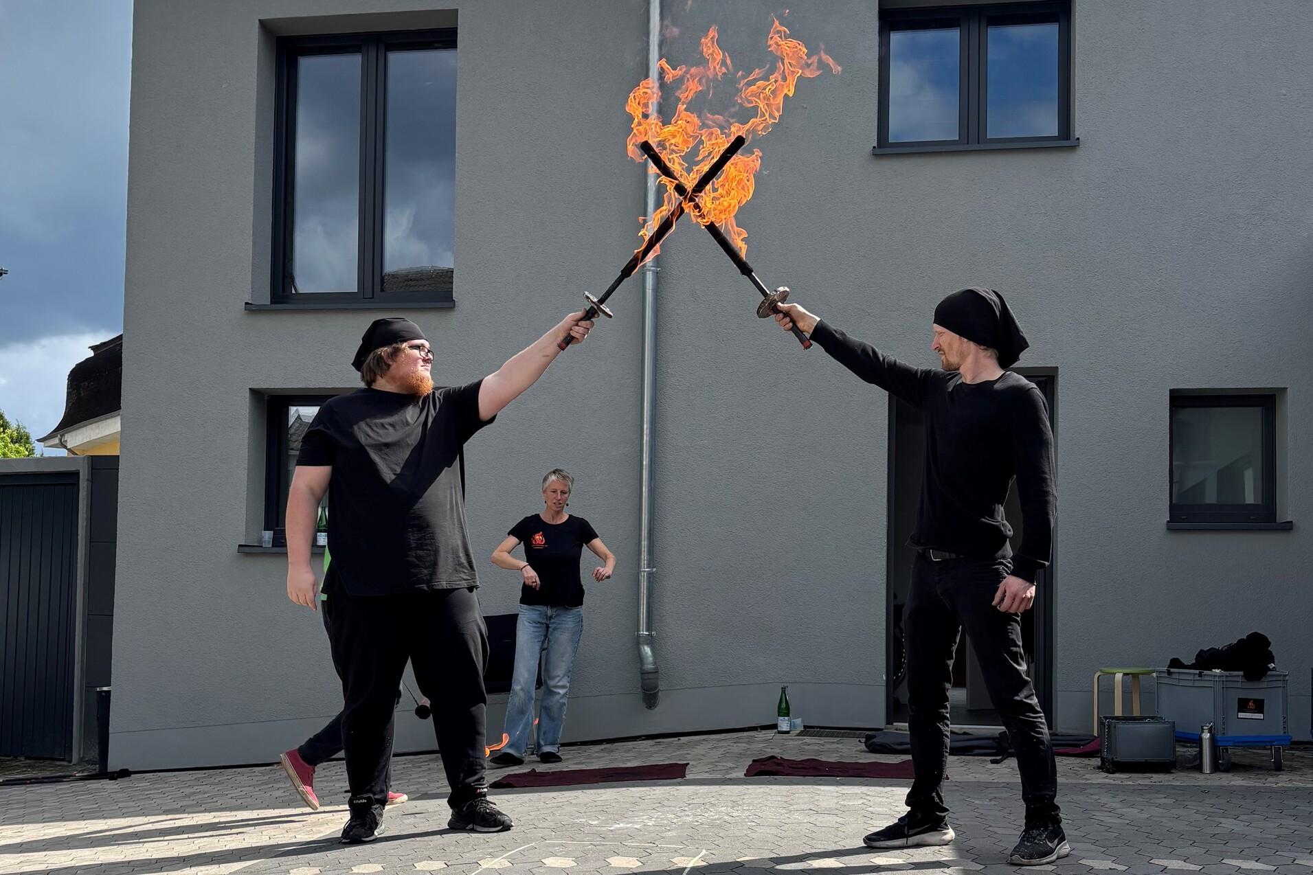 Auf dem Bild sieht man zwei junge M&auml;nner mit brennenden Feuerschwertern